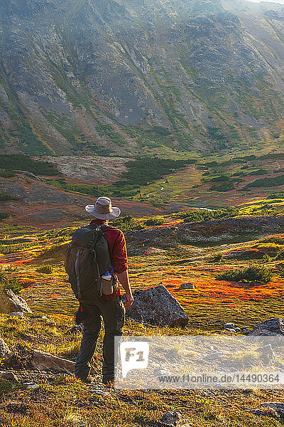 A man backpacking is hiking up the Hidden Lake Trail in the Chugach State Park on a sunny fall day in Southcentral Alaska.