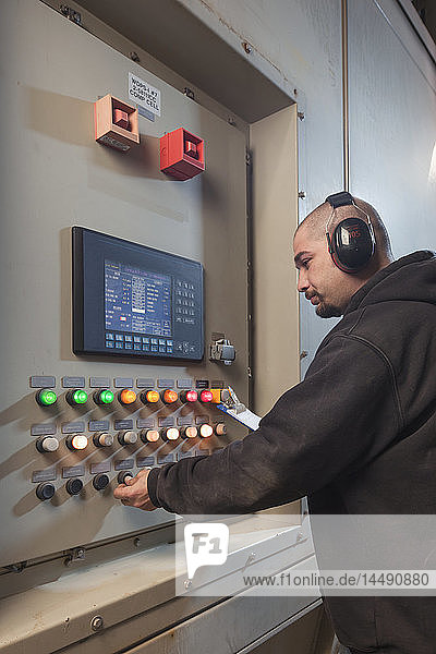 Ein männlicher Arbeiter mit Gehörschutz inspiziert eine Schalttafel eines Elektrizitätswerks, Prudhoe Bay, arktisches Alaska, USA, Sommer