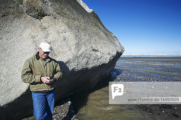 Mann mit Mobiltelefon neben einer großen Felsformation  Clam Gulch  Kenai-Halbinsel  Southcentral Alaska