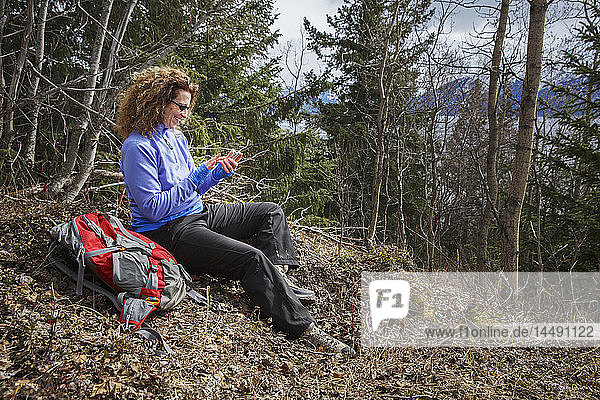 Wanderin  die sich auf dem Bird Ridge am Turnagain Arm ausruht und ein Mobiltelefon benutzt  Southcentral Alaska