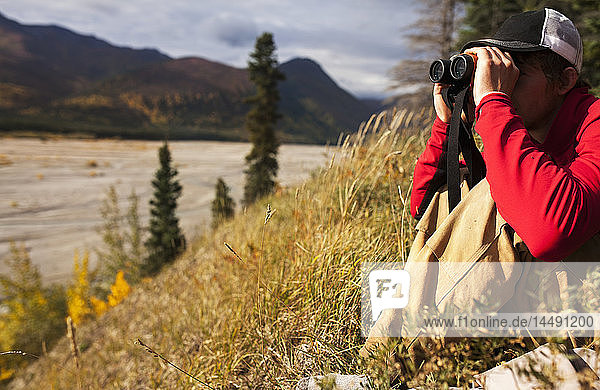 Mann beobachtet ein verzweigtes Flussbett mit einem Fernglas bei der Jagd in der Nähe von Tok  Süd-Zentral-Alaska