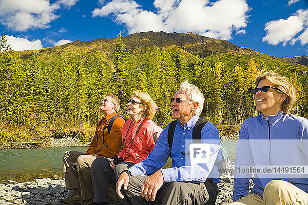 Group of senior hikers rest beside Granite Creek on Kenai Peninsula in Southcentral Alaska during Autumn