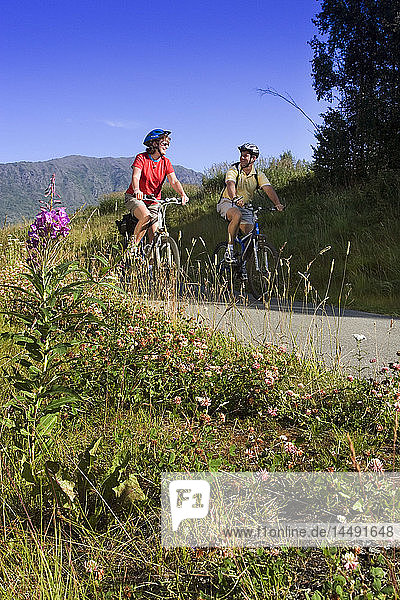 Couple riding bikes together on Coastal Trail near Indian  Alaska  Turnagain Arm  SC Summer.