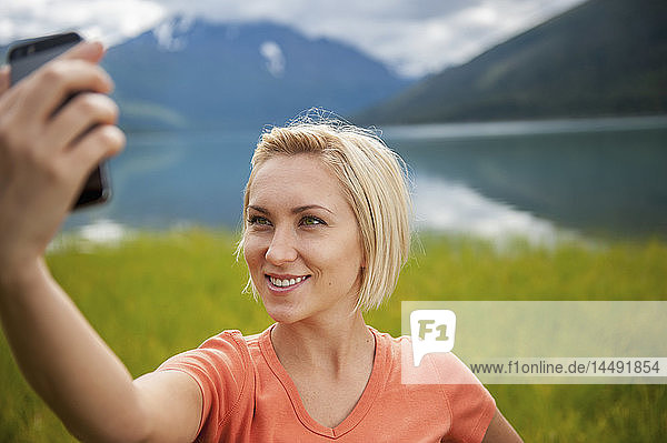 Woman using a smartphone to take a selfie in front of Eklutna Lake  Chugach State Park  Southcentral Alaska
