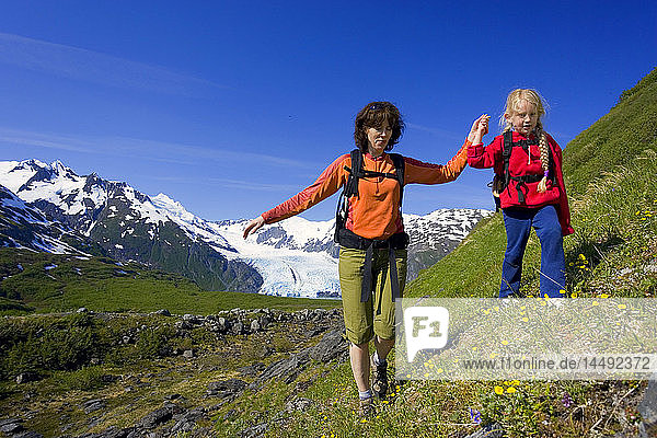 Mother & daughter hiking on steep wildflower covered mountain slope Portage Pass Trail Chugach NF Alaska