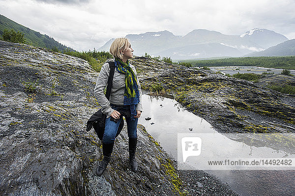 Frau steht auf einer Felsenlandschaft in der Nähe von Seward mit den Kenai Mountains im Hintergrund  Kenai-Halbinsel  Süd-Zentral-Alaska