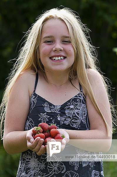 Mädchen hält Erdbeeren und schaut in die Kamera