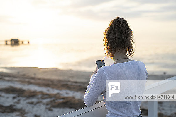 Junge Frau fotografiert Sonnenuntergang am Strand