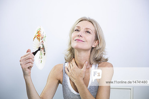 Eine Frau fächelt sich Luft zu  um die Symptome einer Hitzewallung zu lindern.