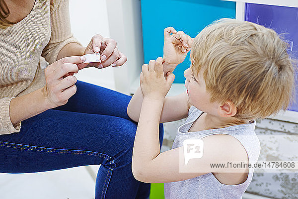 Mother putting adhesive bandage on her son´s arm.