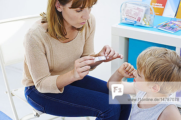 Mother putting adhesive bandage on her son´s arm.