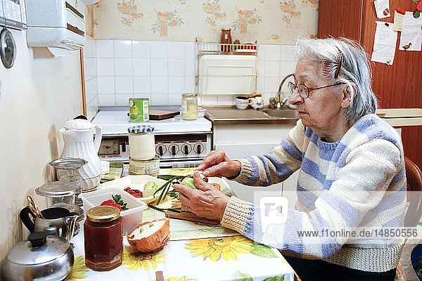 An elderly woman cooking in her home  helped by her daughter who is her guardian.