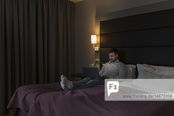 Mann benutzt Laptop im Schlafzimmer