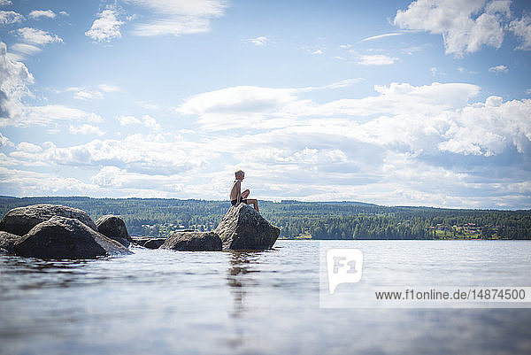 Boy sitting on rock at sea