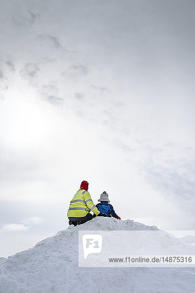 Mutter und Kind sitzen auf einem verschneiten Hügel
