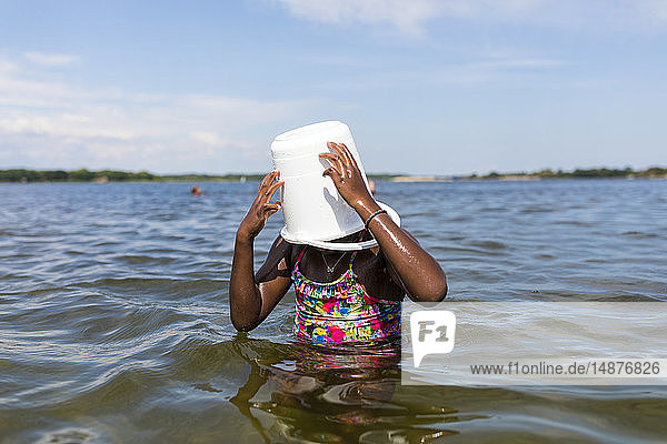 Girl in sea with bucket on her head