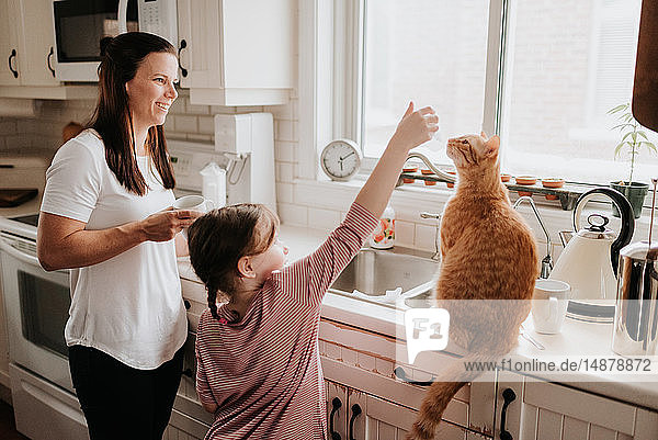 Mutter beobachtet Tochter beim Spielen mit Katze auf Küchenarbeitsplatte