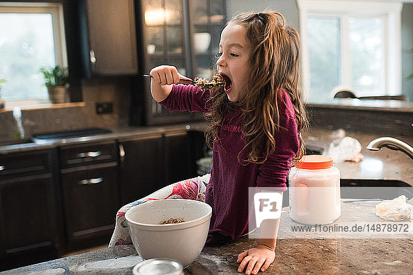 Kleines Mädchen isst auf der Küchenarbeitsplatte