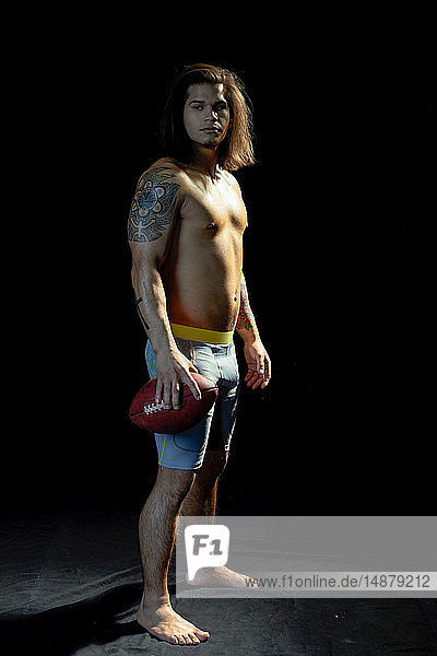 Portrait of bare chested young man with football  black background