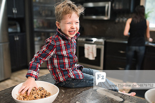 Kleinkind greift frisch gebackene vegetarische Saatkugeln aus Schüssel auf Küchenarbeitsplatte