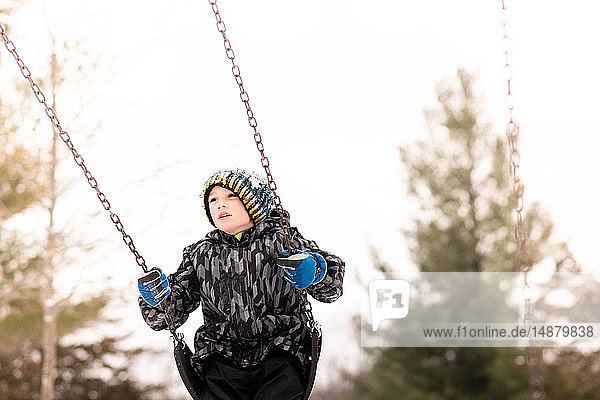 Boy in knit hat swinging on playground swing in winter
