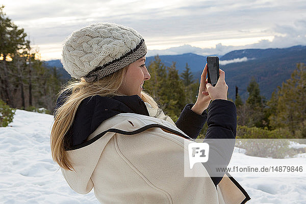 Young woman taking smartphone selfie in winter forest  Twain Harte  California  USA