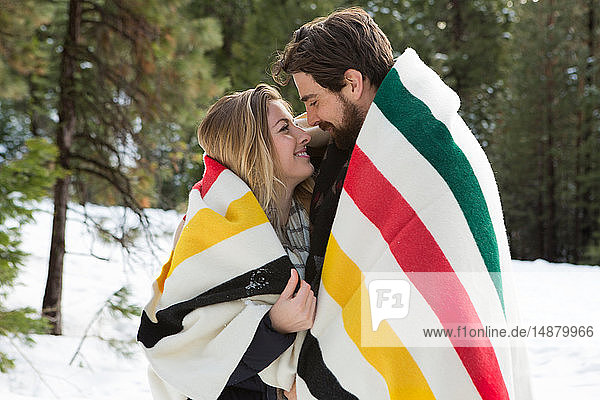 Junge Frau und Freund zusammen in eine Decke gehüllt im Winterwald  Twain Harte  Kalifornien  USA