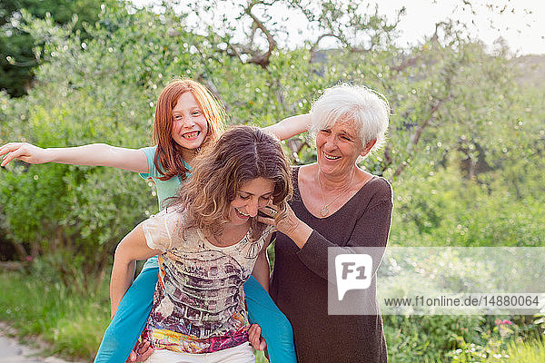 Girl getting piggyback with mother and grandmother in garden