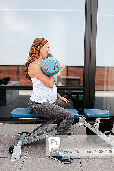 Schwangere Frau mit Gewichten auf dem Balkon