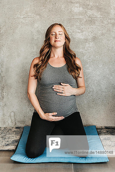 Schwangere Frau auf Yogamatte neben Betonwand