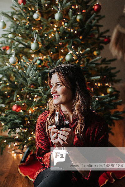 Frau trinkt Wein neben geschmücktem Weihnachtsbaum