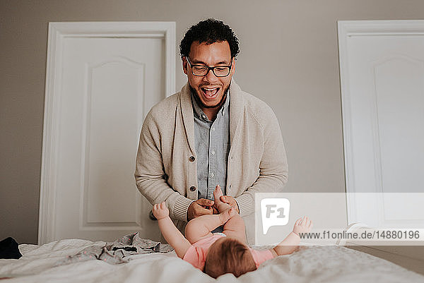 Father dressing baby daughter on bed in bedroom