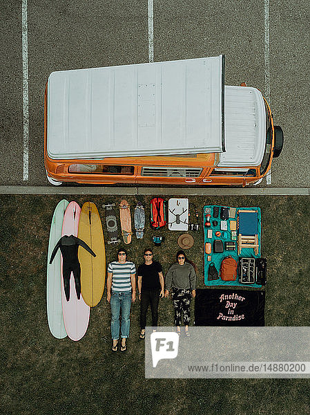 Drei junge Surfer mit Surfausrüstung und Freizeitfahrzeug auf dem Rücken liegend am Strandparkplatz  Portrait von oben  Ventura  Kalifornien  USA