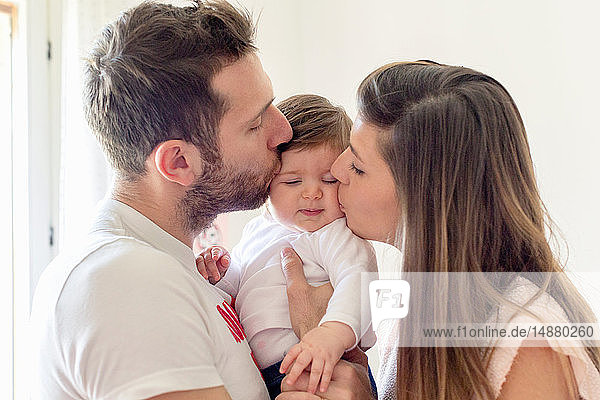 Parents kissing baby girl's cheeks at home