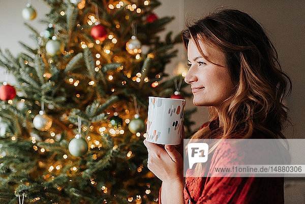 Frau trinkt Kaffee neben geschmücktem Weihnachtsbaum