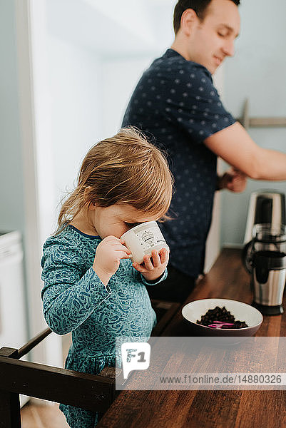 Weibliches Kleinkind mit Vater trinkt aus Tasse an der Küchentheke