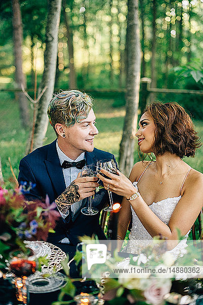 Braut und Bräutigam erheben ein Glas am Waldtisch