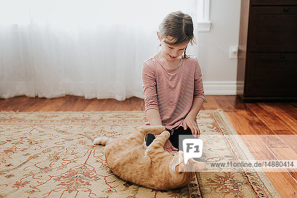 Girl playing with cat on carpet at home