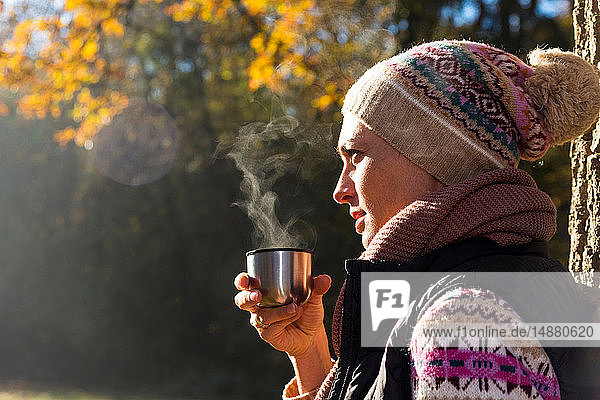 Frau trinkt warmes Getränk im Herbstwald