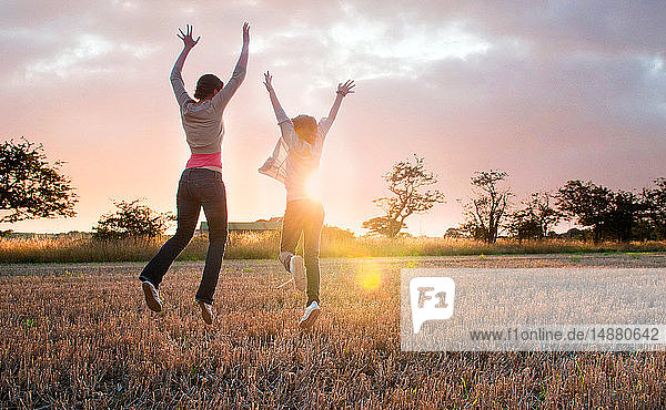 Zwei Mädchen springen vor Freude im sonnenbeschienenen Feld  Rückansicht