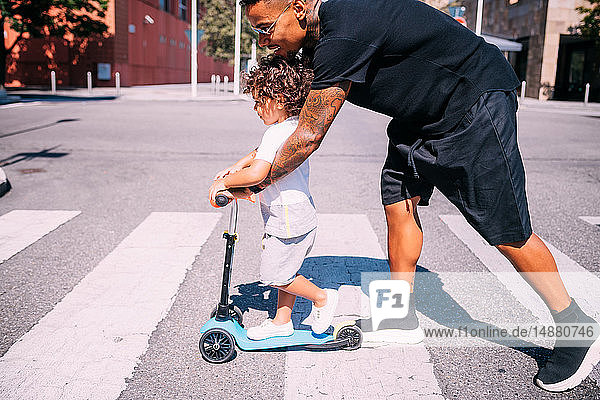 Father teaching son ride push scooter on pedestrian crossing