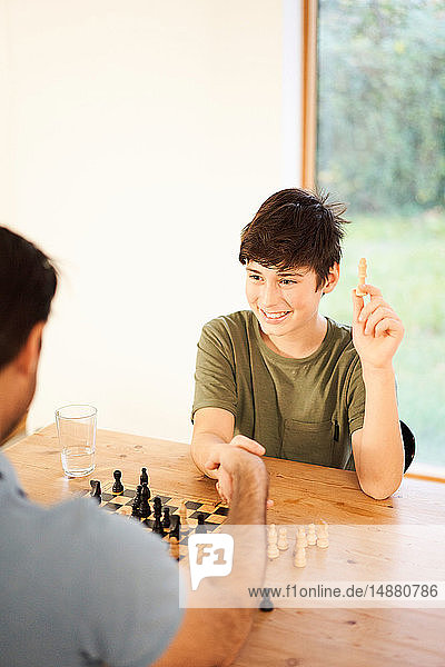Junge und Vater schütteln sich die Hand beim Schachspiel am Wohnzimmertisch  Blick über die Schulter