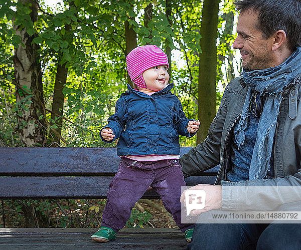 Father and baby girl on park bench by forest