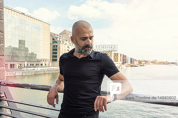 Man looking at smartwatch on bridge  river and buildings in background  Berlin  Germany