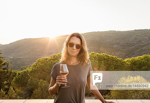 Reife Frau hält ein Glas Wein bei Sonnenuntergang, Porträt, Portoferraio, Toskana, Italien