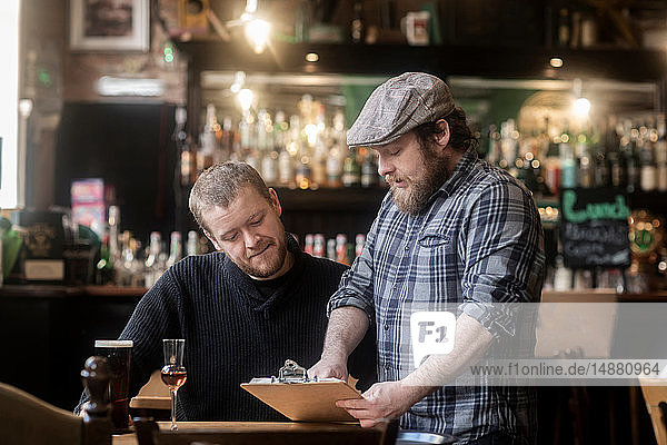 Barman looking at menu with customer in traditional Irish public house