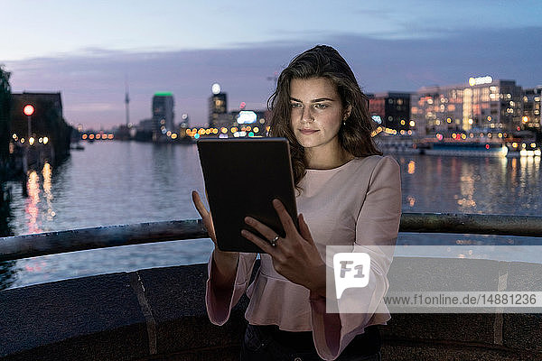 Junge Frau mit digitalem Tablett auf Brücke  Fluss und Stadt im Hintergrund  Berlin  Deutschland