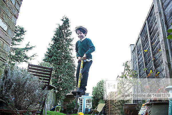 Junge springt auf Pogo-Stock im Garten