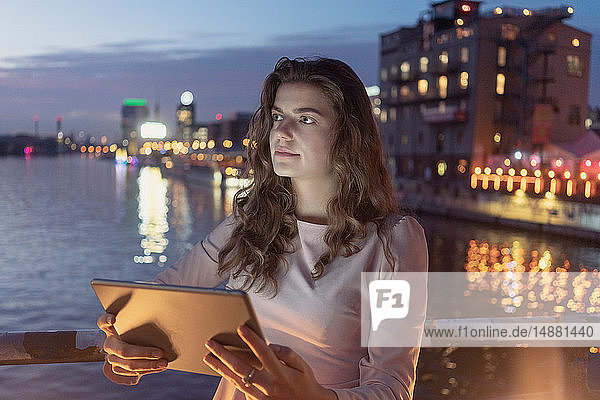 Junge Frau mit digitalem Tablett auf Brücke Fluss und Stadt im Hintergrund Berlin Deutschland
