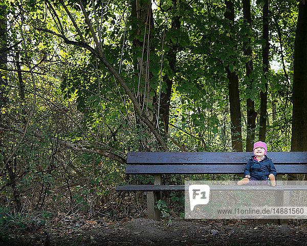 Smiling baby girl on park bench by forest